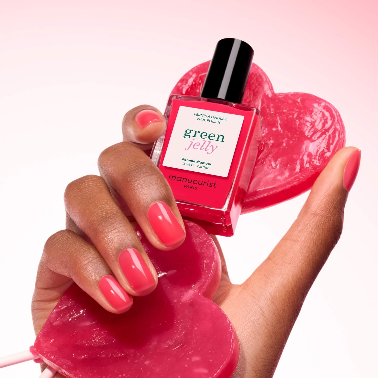 A hand with pink manicured nails holds a heart-shaped soap and a bottle of Manucurist Pomme d&