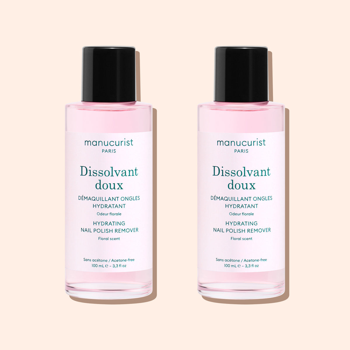 Two bottles of Manucurist Gentle Remover, an acetone-free nail polish remover with pink liquid, are side by side on a beige background. Each has a black cap and white label with text.