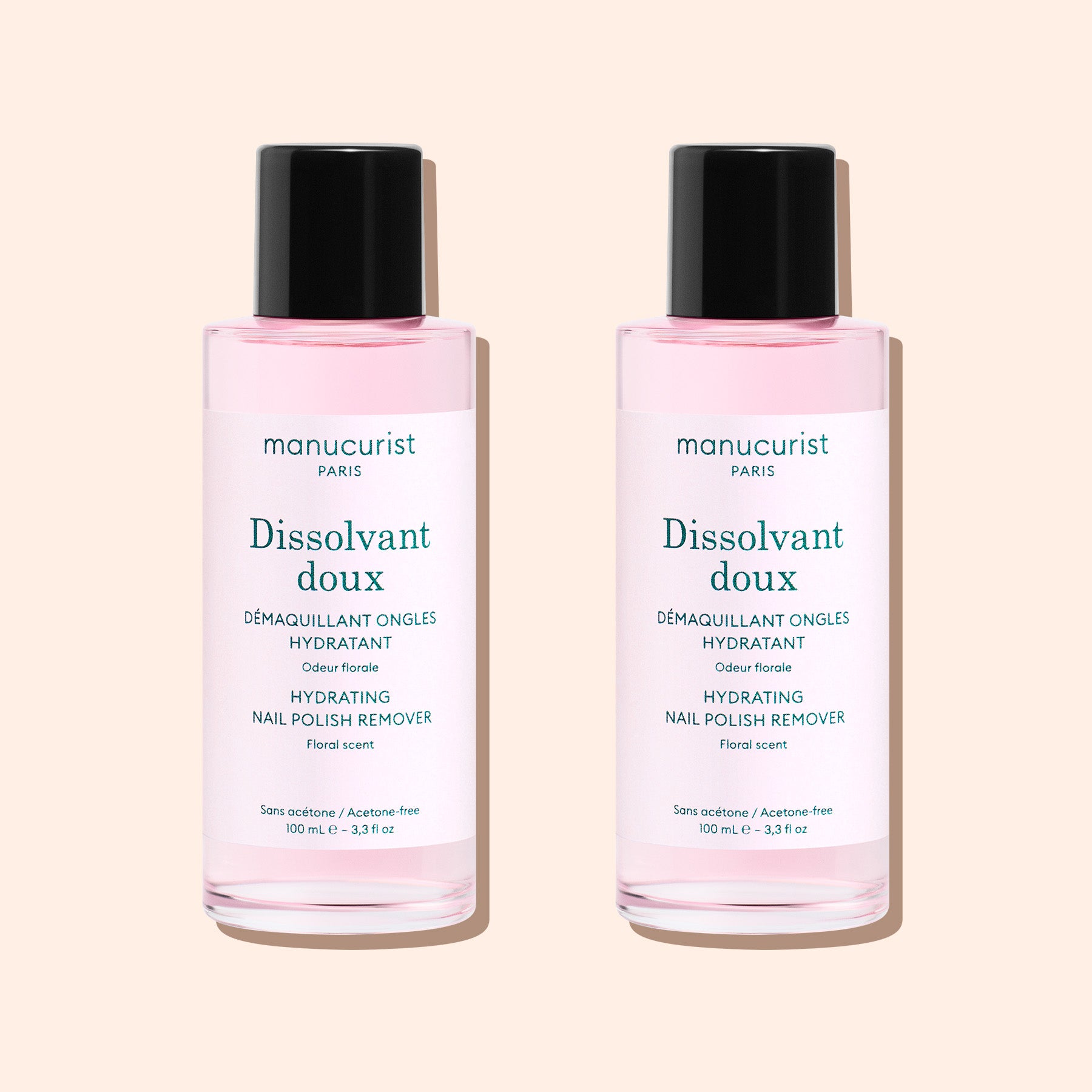 Two bottles of Manucurist Gentle Remover, an acetone-free nail polish remover with pink liquid, are side by side on a beige background. Each has a black cap and white label with text.