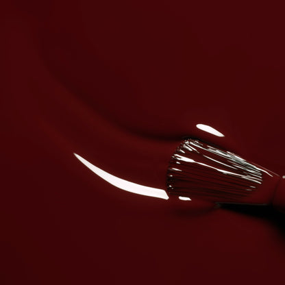 A close-up of a brush spreading Grenat, an earthy red nail polish from Manucurist’s Green™ range, with light reflecting off the smooth, glossy surface.