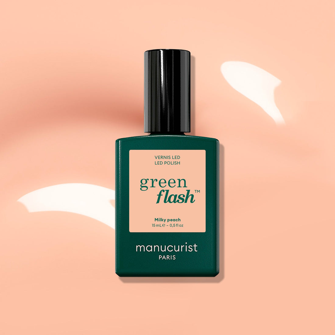 A green bottle of Manucurist Milky Peach Green Flash LED nail polish rests on a peach-hued background with glossy highlights, highlighting the ideal milky peach gel shade from Manucurist for those desiring a subtle yet elegant manicure.