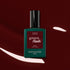 A bottle of Manucurist Grenat gel polish, set against a glossy earthy red nail polish background with white highlights.