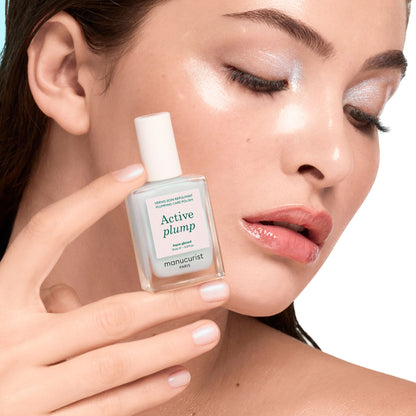 A woman with glowing, dewy skin and shimmery eye makeup holds Manucurist&