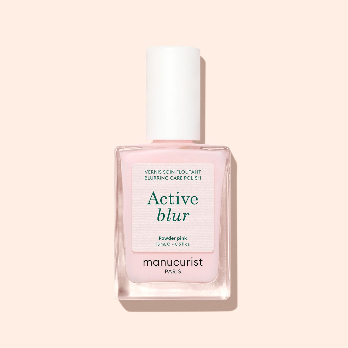 A bottle of Manucurist Active™ Blur nail polish, a blurring care polish in powder pink that provides a soft matte finish, is photographed against a light beige background.