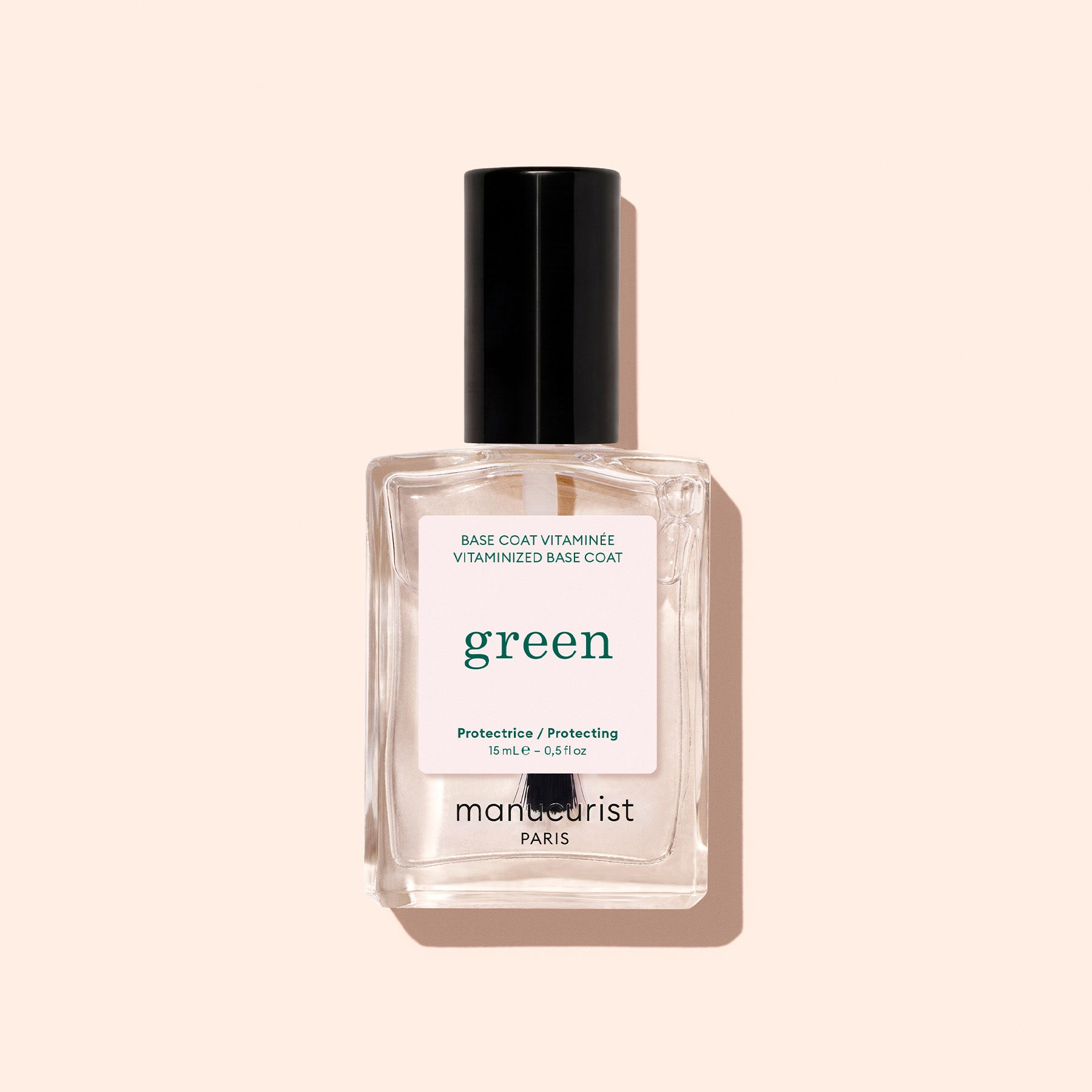 A clear glass bottle of Manucurist Vitaminised Base Coat Green™ with a black cap, set against a light beige background. It uses KeraHCE+ technology to strengthen nails and create a smooth base for color.