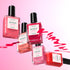 Six bottles of Manucurist Rainbow Collections nail polish in pink, red, and orange float on a pink gradient background with swirling colors—ideal for trendy manicures and curated colour palettes.