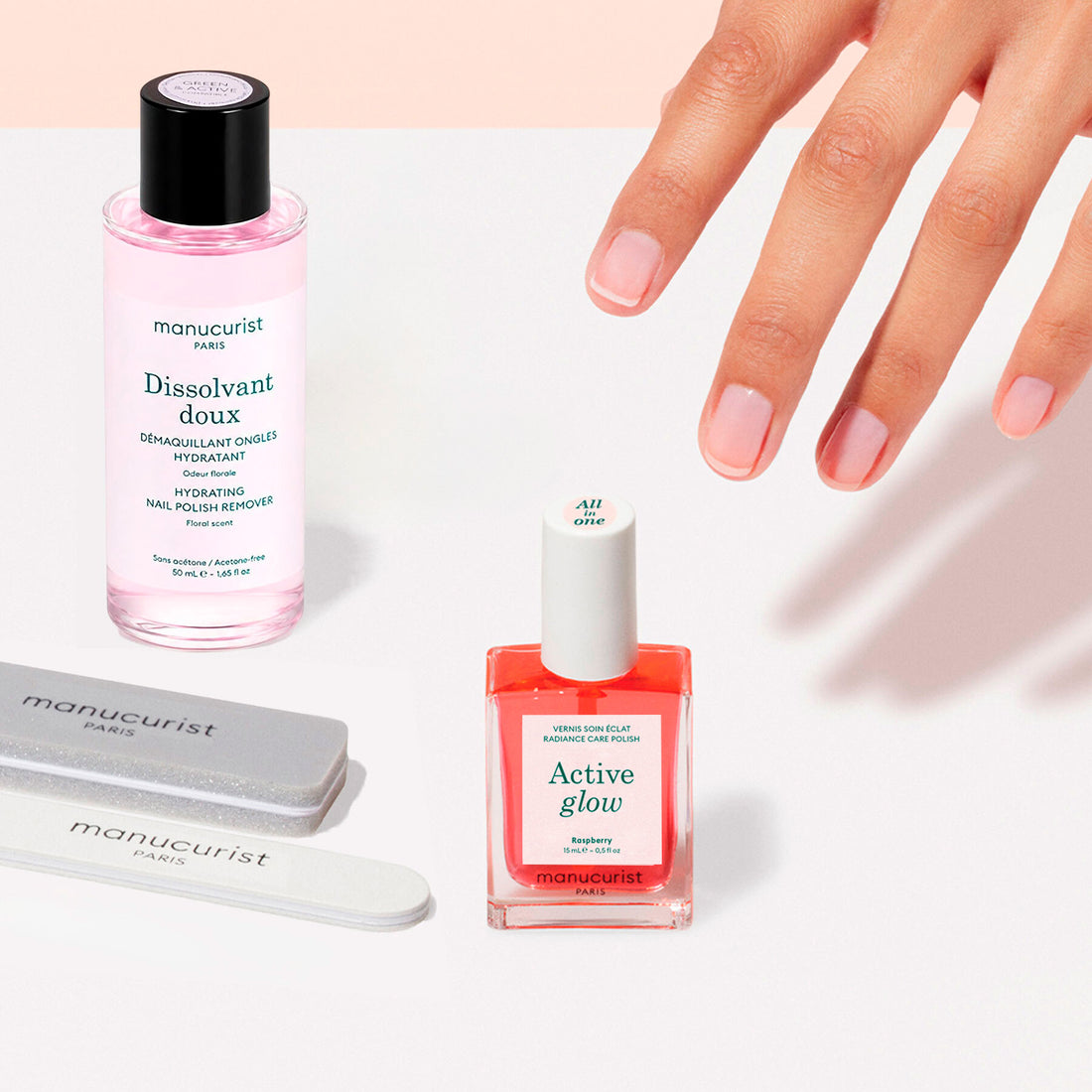 A hand with neatly manicured nails is shown beside the Manucurist Active™ Discovery Kit, featuring a bottle of remover, a bottle of nail polish, and two nail files—all arranged on a light surface—providing an ideal setup for maintaining your nail care routine and ensuring healthy, hydrated nails.