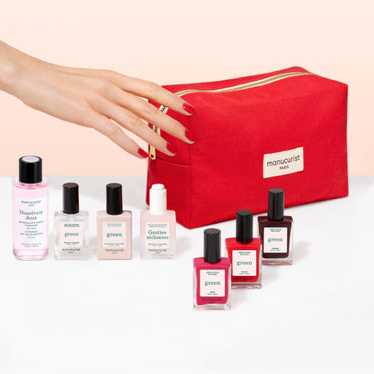 A hand with painted nails holds the Manucurist Starter Kit—a red manicure bag made from organic cotton. In front are six gel-effect nail polishes in assorted shades, a nail polish remover bottle, and the bag is labeled "manucurist PARIS.