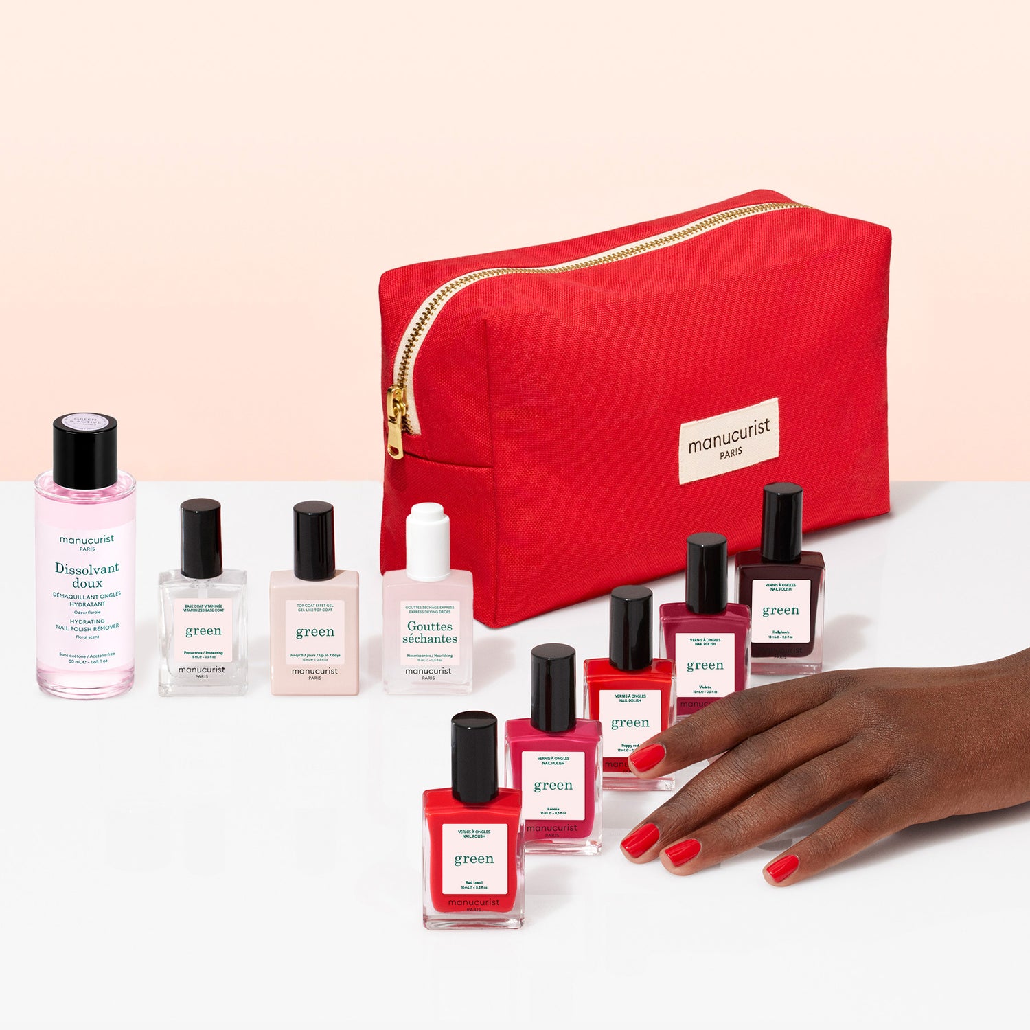 A hand with red nails rests in front of the Manucurist Super Starter Kit, featuring seven plant-based nail polish bottles, a remover, a nail care bottle, a cuticle serum, and a red Manucurist Paris pouch—everything you need for the perfect gel effect manicure.