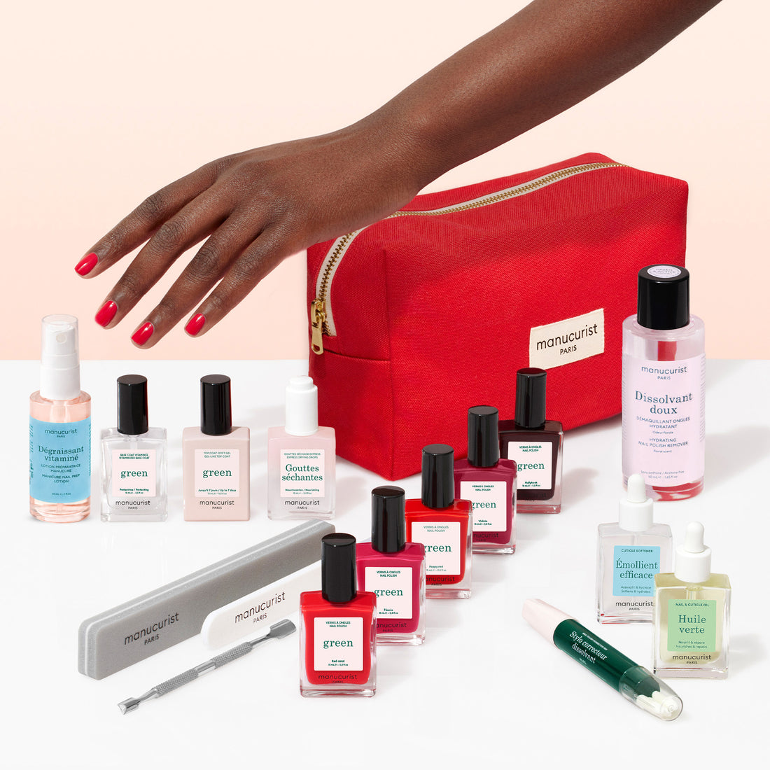 A hand with red manicured nails reaches toward a green Super Addict Kit containing bottles of polish, a nail file, a pusher, and a red zippered pouch.
