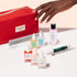 A hand reaches toward the Manucurist Active™ Ultimate Manicure Kit—a red nail care set featuring files, serums, polish bottles, cuticle remover, and a cuticle pen—each product designed to promote healthy nails and elegantly displayed on a light background.