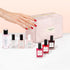A hand with red nail polish reaches toward a pink Manucurist Starter Kit cosmetic bag, surrounded by various bottles of Manucurist gel-effect nail polish and nail care products arranged in front of the bag.