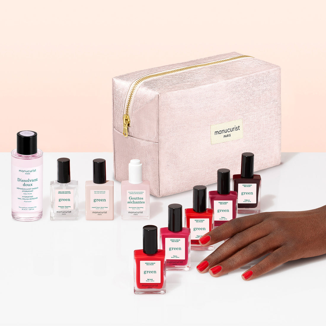 A hand with red nail polish is shown near manicure products, including Manucurist gel-effect nail polishes in various shades, bottles of nail care solutions, and a pink zippered bag labeled Manucurist. The Manucurist Super Starter Kit provides everything you need for flawless nails, all neatly organized in an organic cotton pouch.