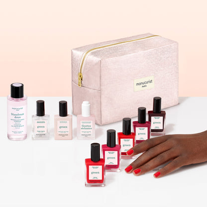A hand with red nail polish is shown near manicure products, including Manucurist gel-effect nail polishes in various shades, bottles of nail care solutions, and a pink zippered bag labeled Manucurist. The Manucurist Super Starter Kit provides everything you need for flawless nails, all neatly organized in an organic cotton pouch.