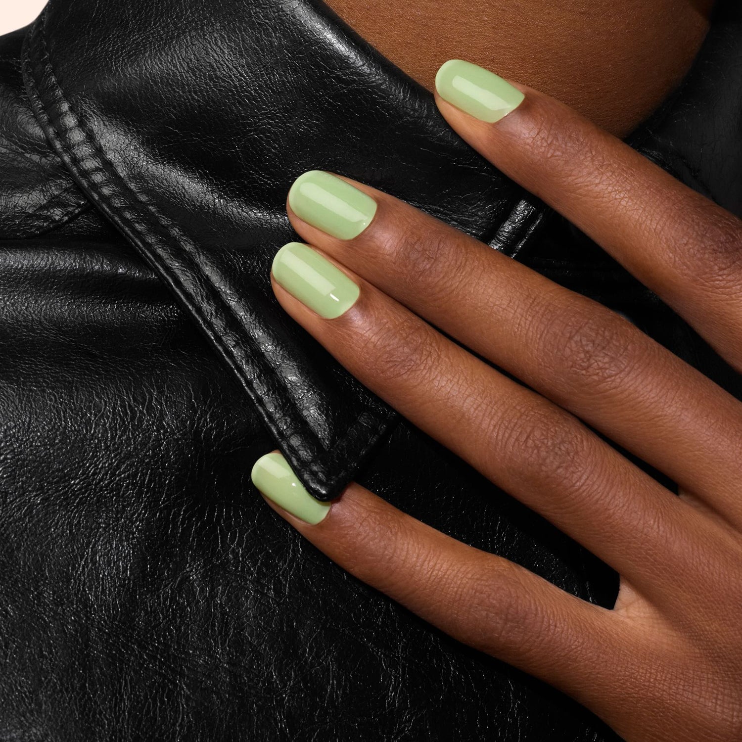 A hand with Manucurist’s Milky Matcha nail polish from The Green range rests on the collar of a black leather jacket.