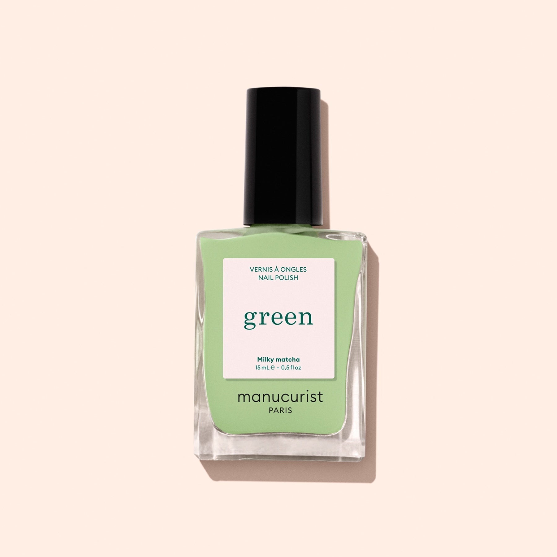 A bottle of Manucurist’s Milky Matcha nail polish, distinguished by its sleek black cap and delicate botanical hues, from The Green range, is displayed against a light beige background.
