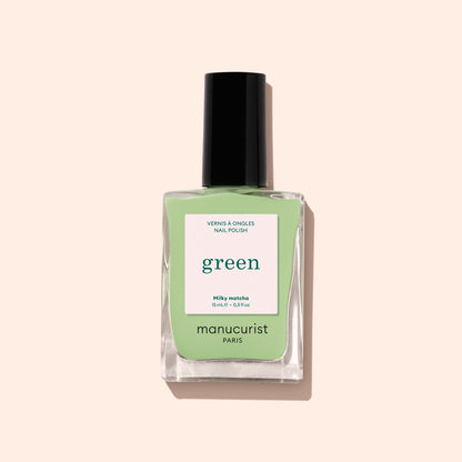A bottle of Manucurist’s Milky Matcha nail polish, distinguished by its sleek black cap and delicate botanical hues, from The Green range, is displayed against a light beige background.