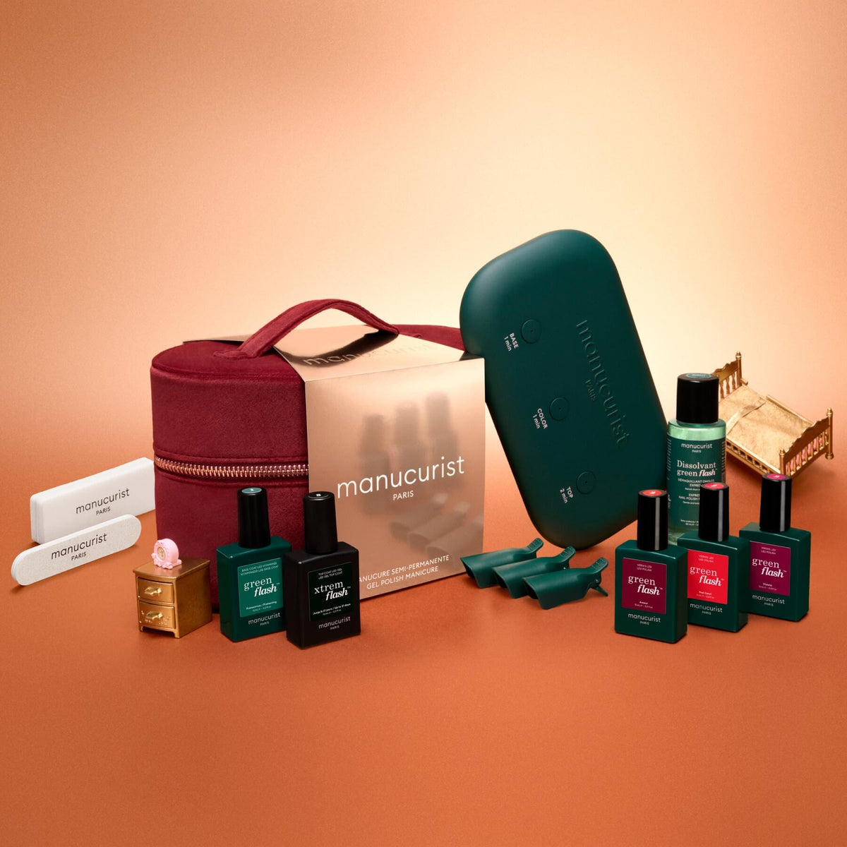 A burgundy carrying case for the Manucurist Green Flash™ Starter Kit Gift Set, featuring an LED lamp, several bottles of polish, remover, files, and clips for salon-style nails at home.