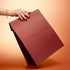 A hand with polished nails holds the Manucurist Holiday Gift Bag - M against a warm gradient background.