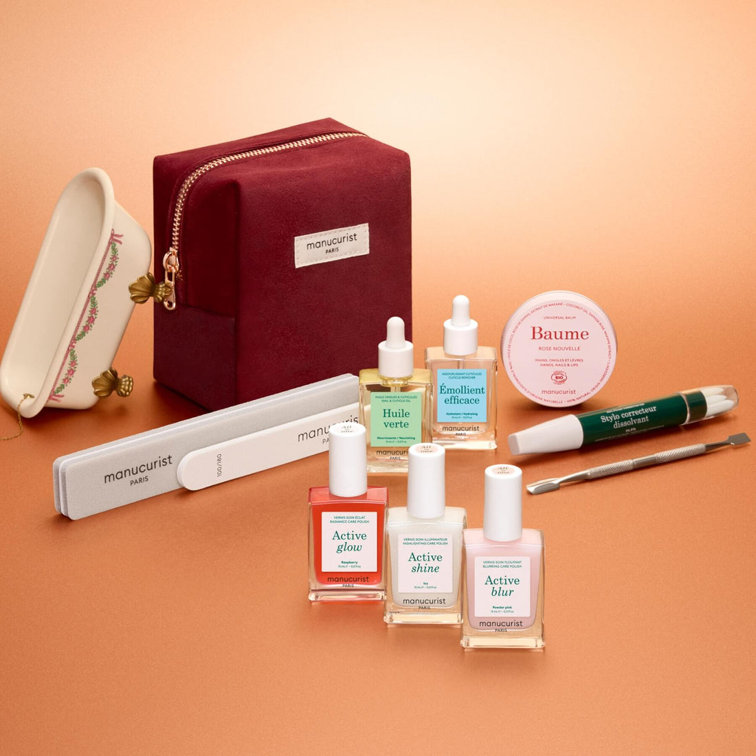 The Manucurist Active™ Ultimate Kit Gift Set featuring three bottles of nail polish, two dropper bottles of cuticle oil, a jar of balm, a nail file, a corrective pen, and a metal tool arranged in front of a zippered pouch.