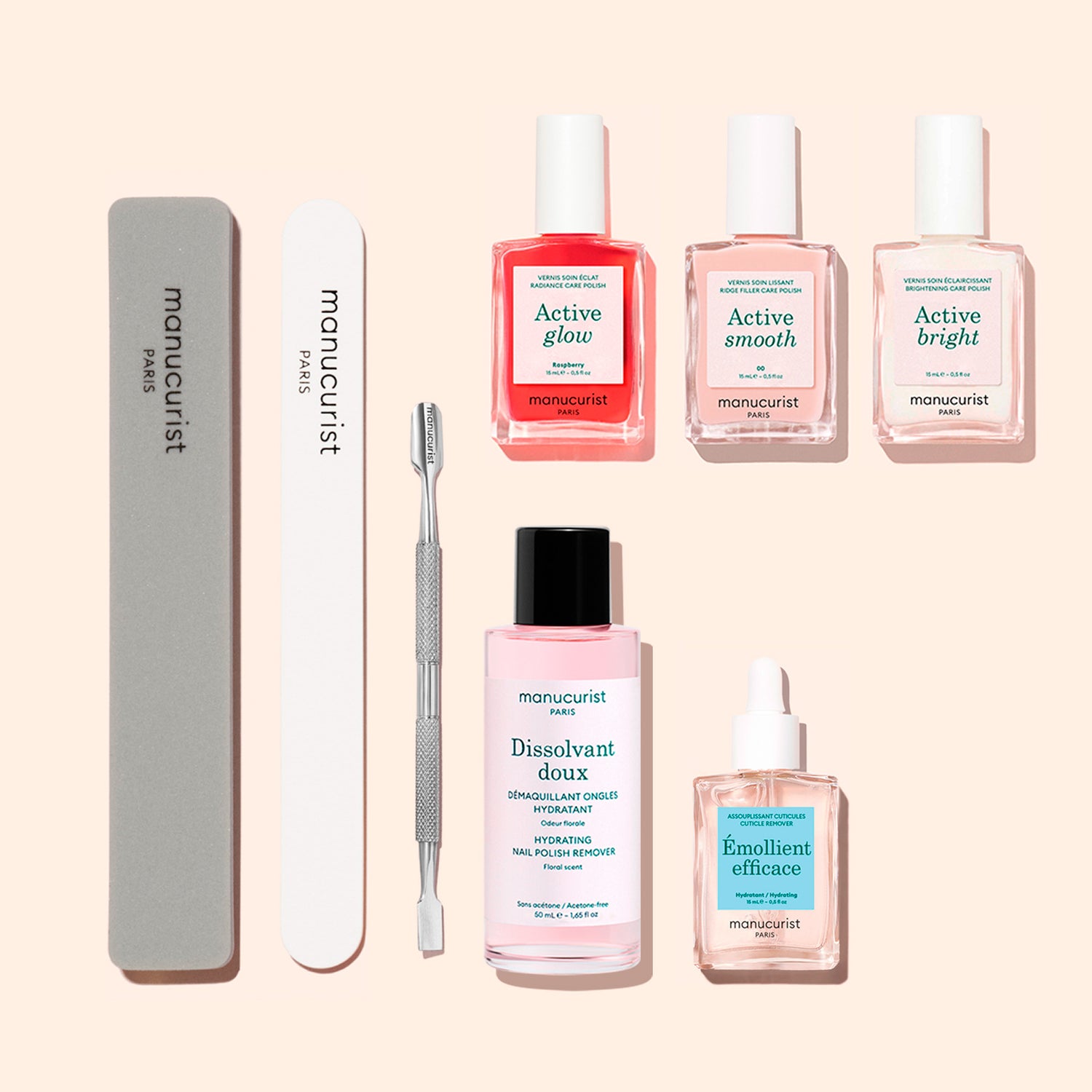 The Manucurist Active™ Manicure Kit, featuring three nail polishes, a remover, a nourishing nail serum, a nail oil, a metal cuticle pusher, a gray nail file, and a white buffer from Manucurist, is arranged neatly on a beige background.