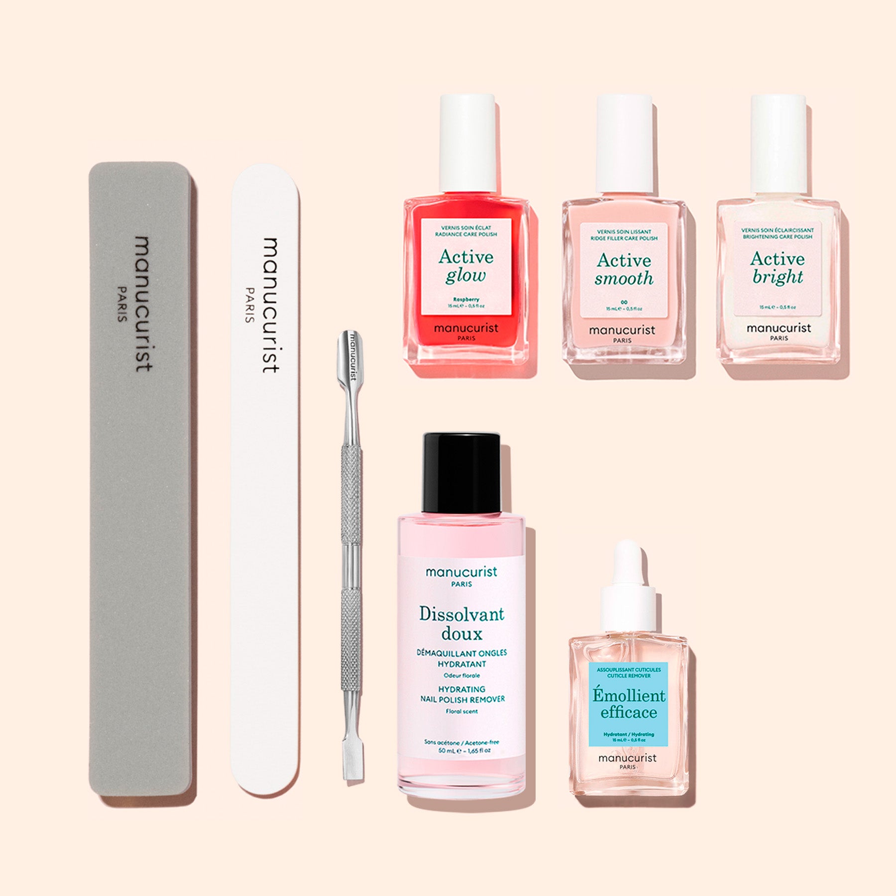 The Manucurist Active™ Manicure Kit, featuring three nail polishes, a remover, a nourishing nail serum, a nail oil, a metal cuticle pusher, a gray nail file, and a white buffer from Manucurist, is arranged neatly on a beige background.