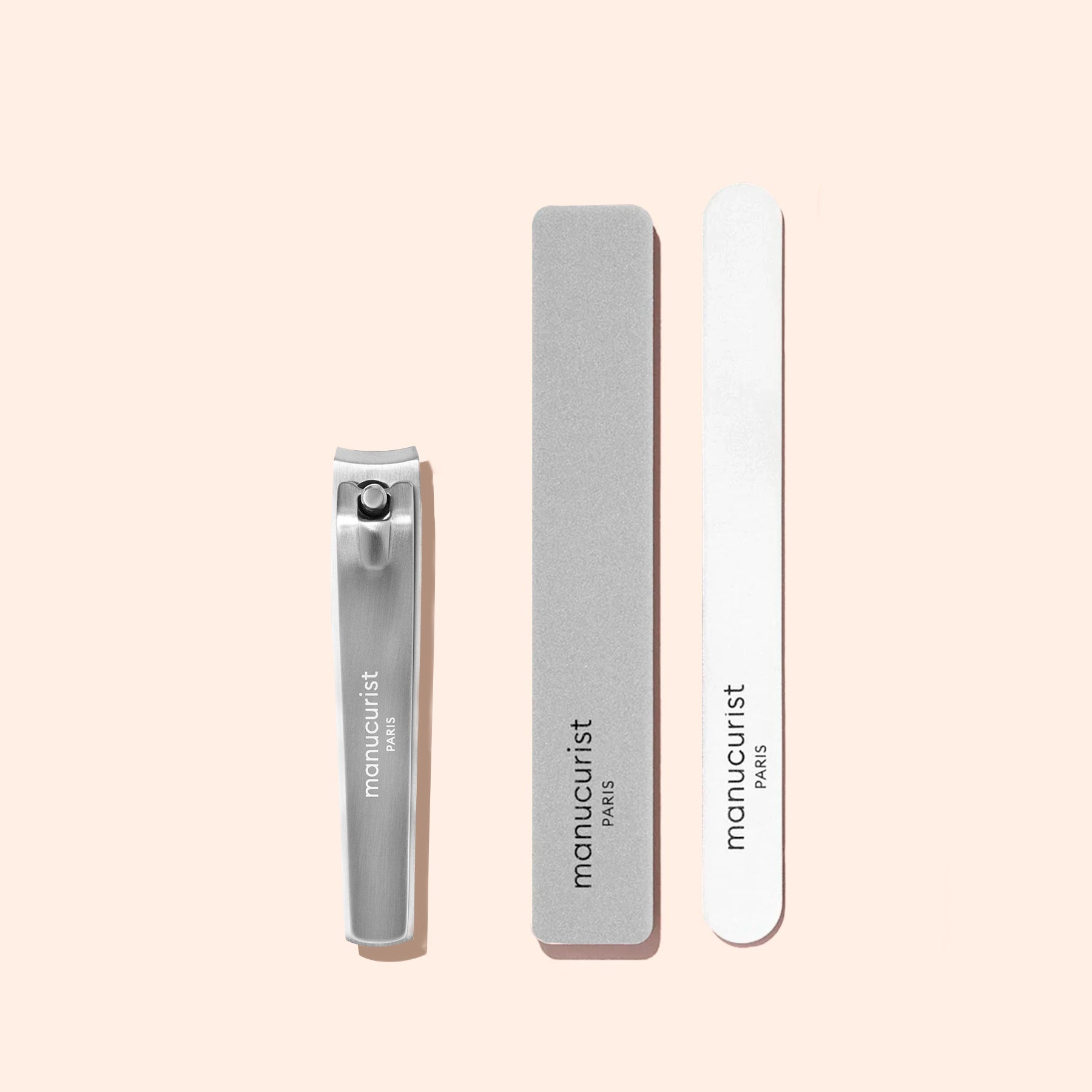 A Manucurist Nail Clipper accompanied by two nail files—one gray, one white—each labeled with the brand name, arranged neatly on a light beige background for the ideal natural nail care and a flawless manicure.