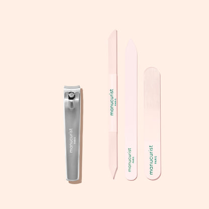 A Manucurist Nail Clipper in silver and three light pink nail files are arranged vertically on a pale pink background, each labeled “Manucurist Paris” in green text—perfect for achieving flawless natural nails.