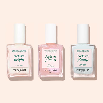 Three square-based nail polish bottles with white caps by Manucurist are shown. Labels read Active Bright (clear), Active Plump (pink), and Active Plump Aqua Glazed (light blue)—volumising care for hydrated nails.