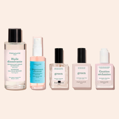 Five nail care products arranged in a row: Manucurist Green Nail Polish Removing Oil, a spray bottle of prep lotion, a clear base coat, a top coat, and a bottle of drying drops.