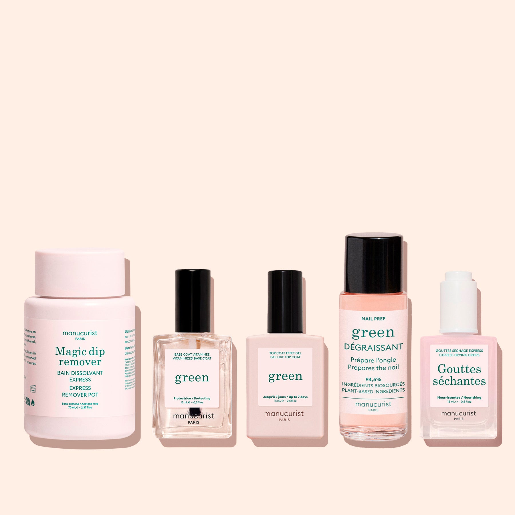 Five Manucurist manicure products are set on a light pink background, including the Magic Dip Remover, two green polishes, a nail prep liquid, and drying drops—all travel-sized with sleek, minimal packaging.
