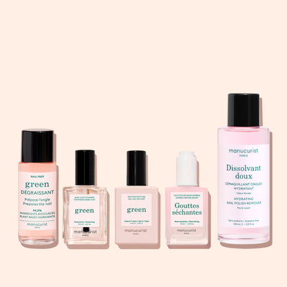 Three Manucurist Green™ products—a base coat, top coat, and nail polish remover—are displayed in glass and plastic bottles against a pale pink background. Labels feature the brand and product names in French and English.
