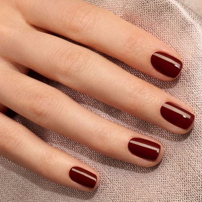 A close-up of a hand resting on a textured fabric surface, with neatly manicured nails painted in Manucurist’s Green™ range shade “Grenat,” showcasing an elegant earthy red.