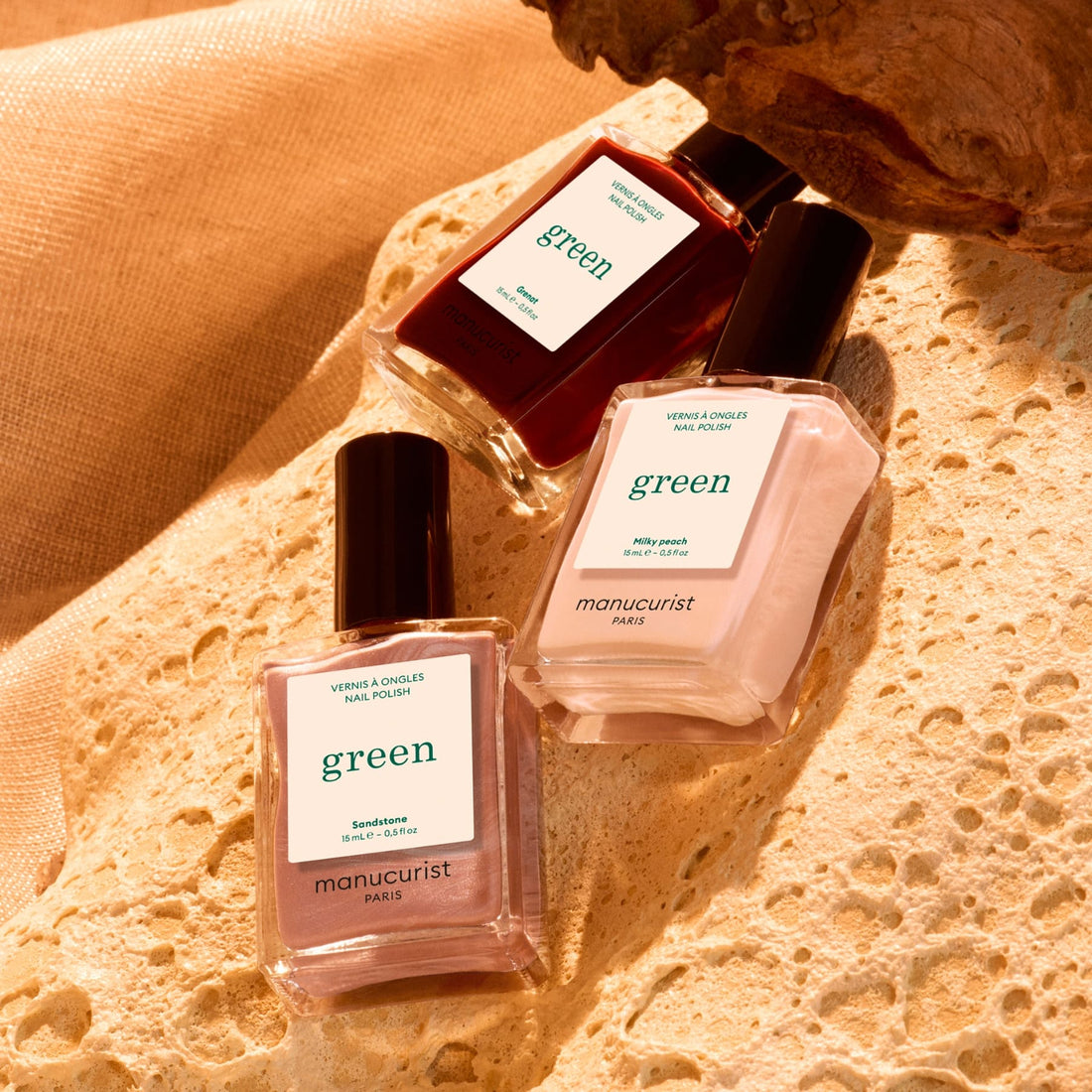 Three bottles from the Manucurist Trio Collections are displayed on a textured beige surface under warm lighting, highlighting curated colour palettes inspired by the latest manicure trends.
