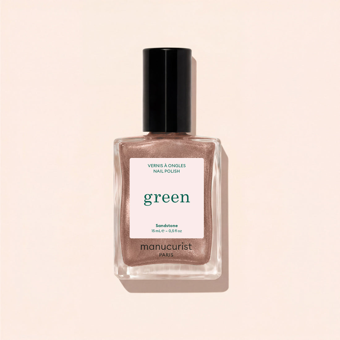 A bottle of Manucurist nail polish in the shade Sandstone is displayed on a light beige surface, with its shadow cast beside it.