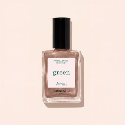 A bottle of Manucurist nail polish in the shade Sandstone is displayed on a light beige surface, with its shadow cast beside it.