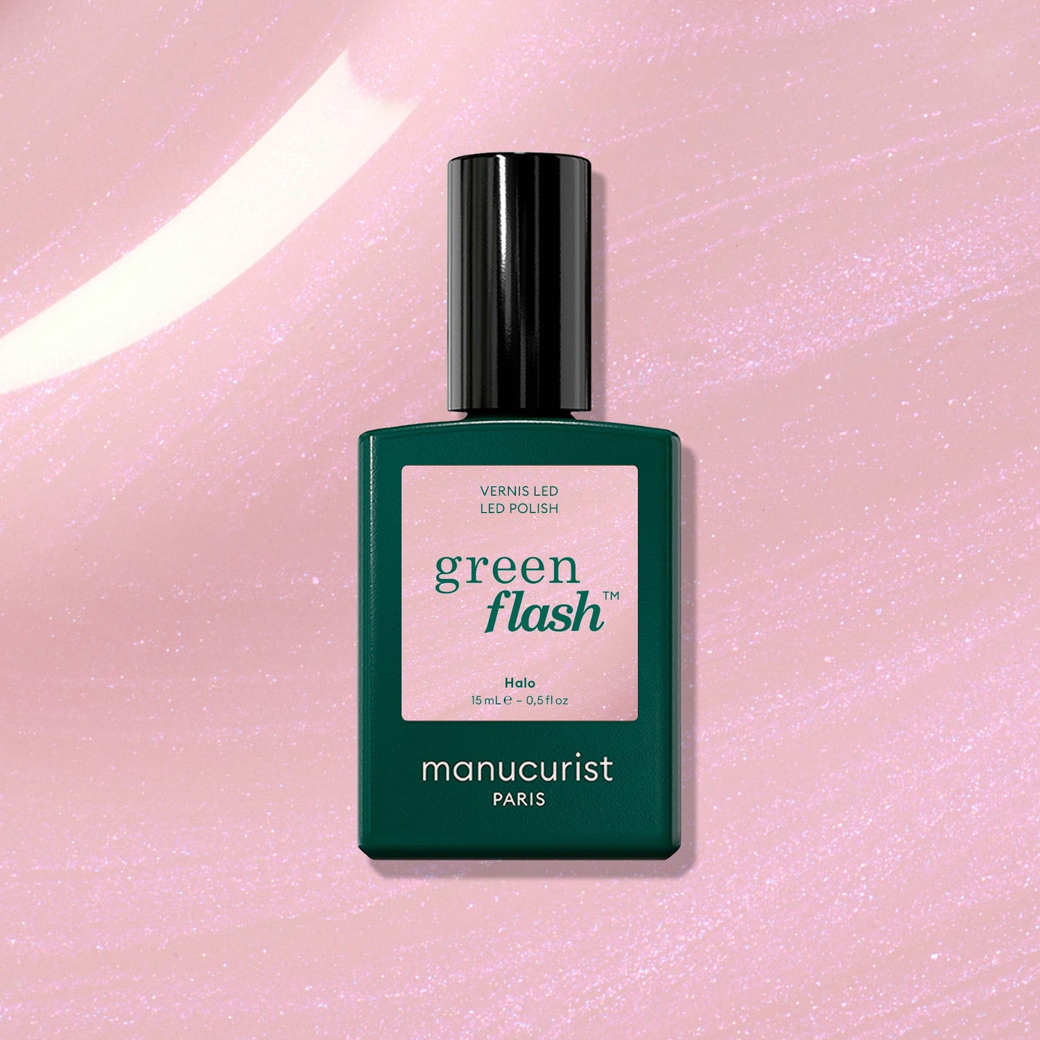 A bottle of Halo gel polish by Manucurist sits on a shimmery pink surface. The dark green bottle features a pink label with the shade name Halo.