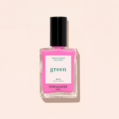 A bottle of Manucurist nail polish in the shade Bloom, neon pink with blue undertones and a black cap, is shown on a light beige background. The label displays “green” and “VERNIS À ONGLES NAIL POLISH.”.