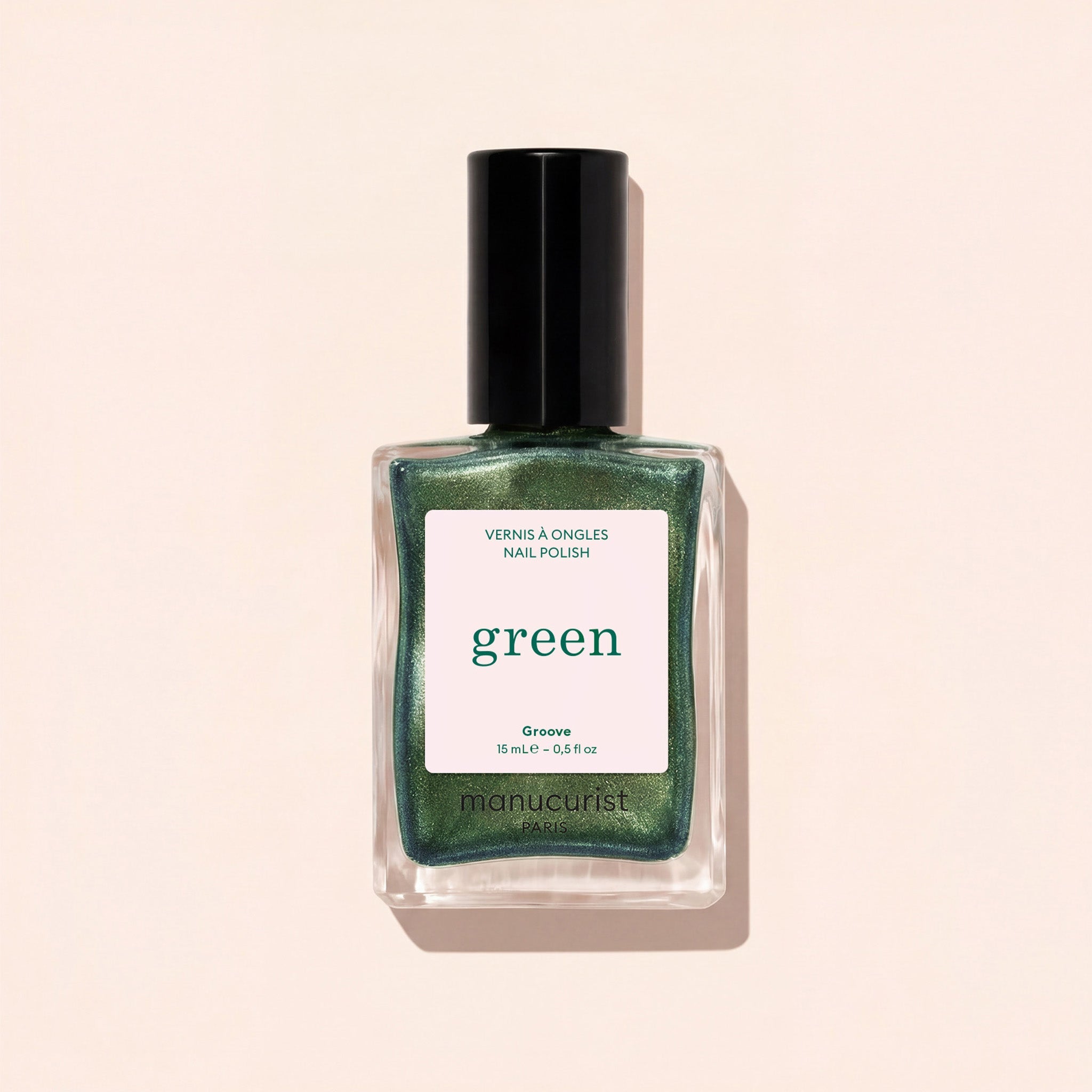 A bottle of Manucurist Groove nail polish in a metallic green shade is displayed against a pale beige background. The label shows "VERNIS À ONGLES NAIL POLISH green Groove 15 ml e .5 fl oz.