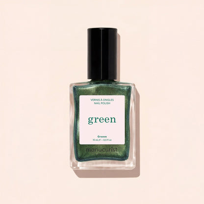 A bottle of Manucurist Groove nail polish in a metallic green shade is displayed against a pale beige background. The label shows "VERNIS À ONGLES NAIL POLISH green Groove 15 ml e .5 fl oz.