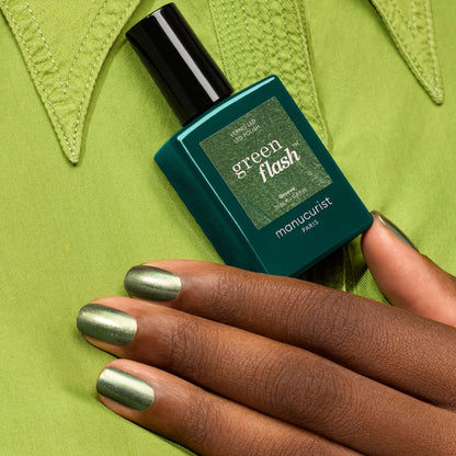 A hand with pearly green nail polish holds a bottle of Groove gel by Manucurist, set against a matching green shirt.