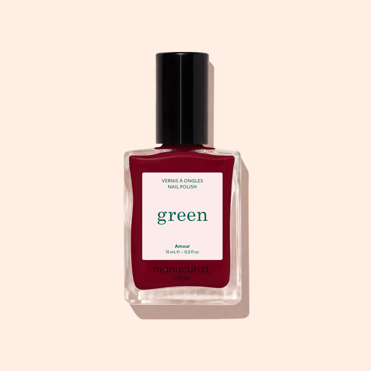 A bottle of Manucurist Amour nail polish from the Paris Green range, featuring a luminous burgundy shade and a black cap, displayed on a light beige background.