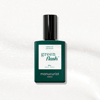 A green bottle of Manucurist gel polish in the shade Bliss rests on a white, slightly textured background. The label displays the shade name “Bliss” and indicates a size of 15 mL.