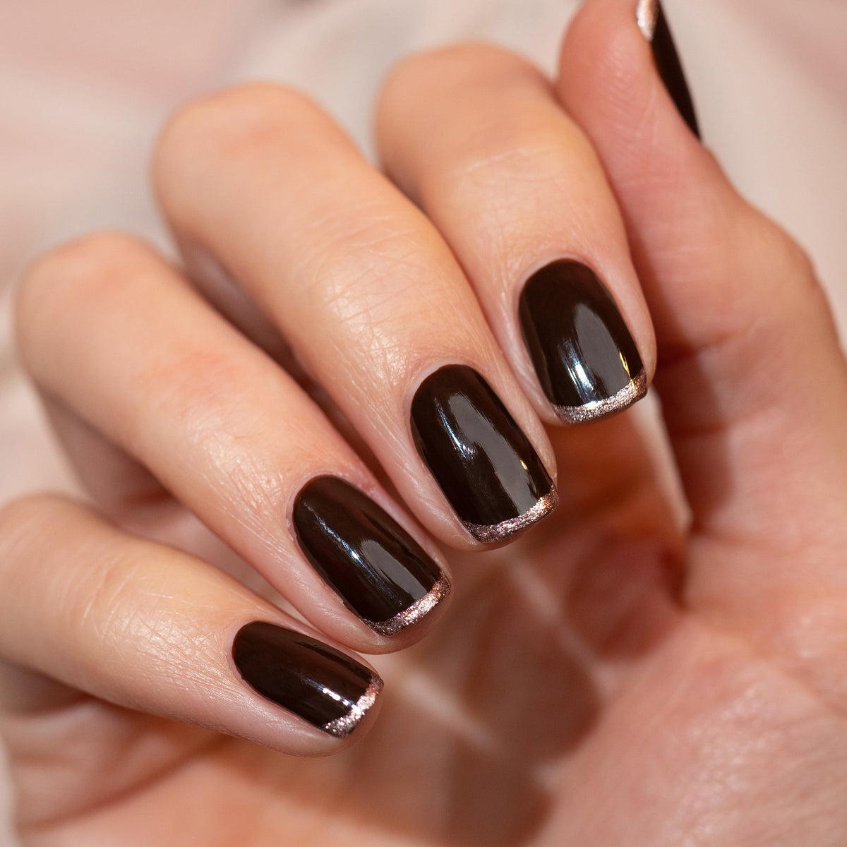 A close-up of a hand with medium-length nails painted in Manucurist’s Clove, a chocolate brown polish with subtle metallic gold tips. The glossy finish highlights the rich tones and elegant style of this look.