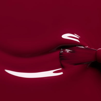 A close-up of a brush applying Manucurist’s Amour gel polish, a luminous, glossy burgundy shade with highlights reflecting on its smooth, shiny surface.
