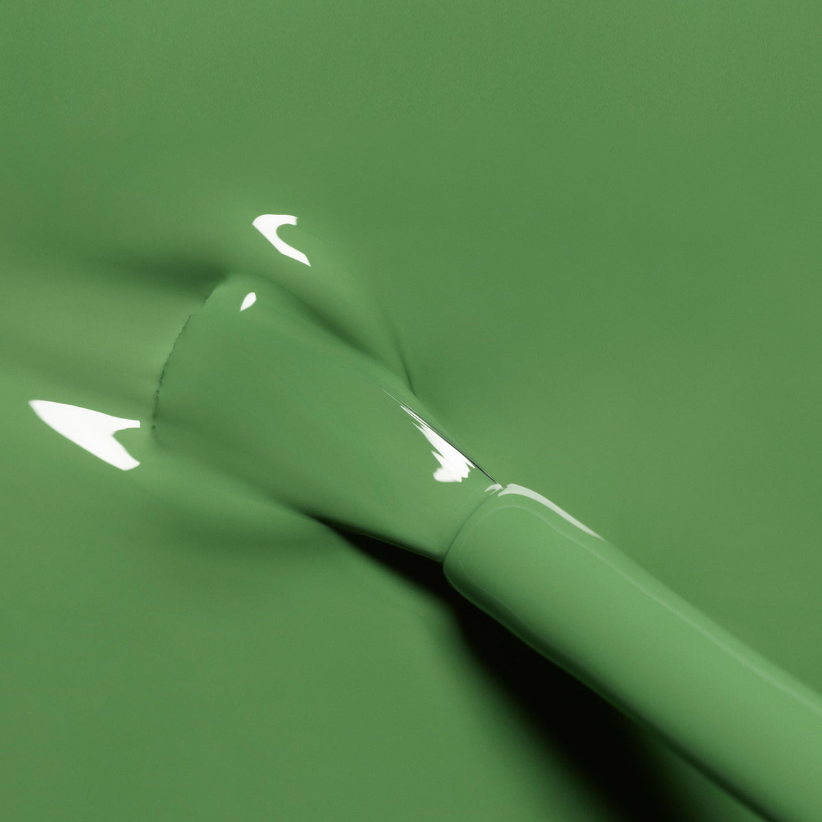 A close-up of a brush applying Manucurist’s Artichoke green nail polish, with light reflections visible on the smooth surface.