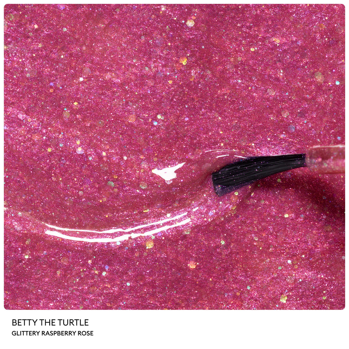 A nail polish brush applies a coat of Petite Manucurist Trio by Manucurist, a sparkly raspberry rose pink children’s nail polish with fine multicolored glitter particles.