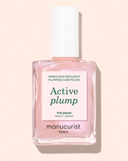 A bottle of Manucurist Active™ Glow Blueberry nail polish, featuring a vibrant blueberry shade and a white cap, set against a pale background. This nail enhancer boasts a plant-based formula for gentle yet effective nail care.
