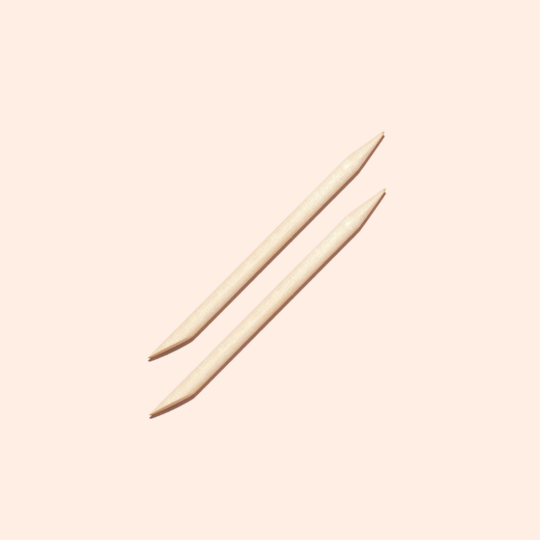 Two Manucurist UK Wooden cuticle sticks (x2), each featuring a pointed tip and a flat angled end for nail cleaning or pushing back cuticles, are arranged parallel to one another on a light beige background.