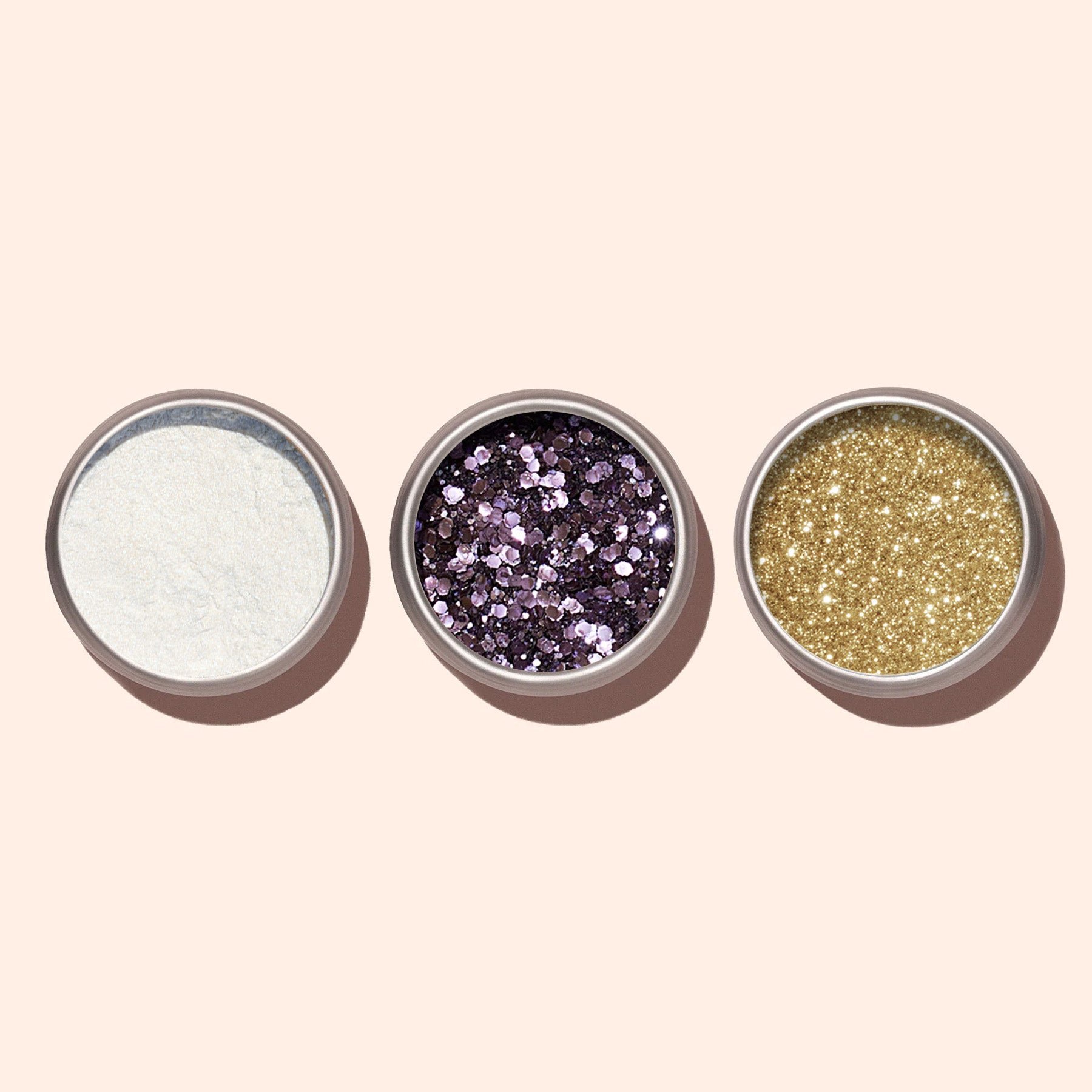 Three small round containers with glitter—one fine white, one chunky Manucurist Lilac biodegradable glitter, and one fine gold—are arranged on a light beige background, ideal for eco-friendly nail art made from plant cellulose.
